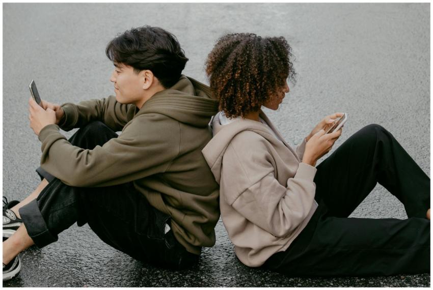 A diverse young couple sits back to back using the