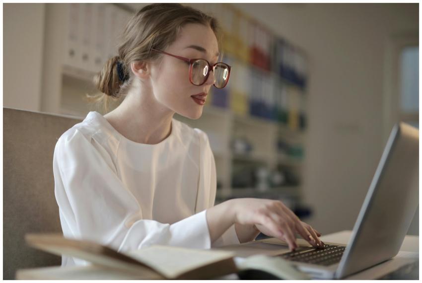 Focused young woman wearing glasses, typing on a l