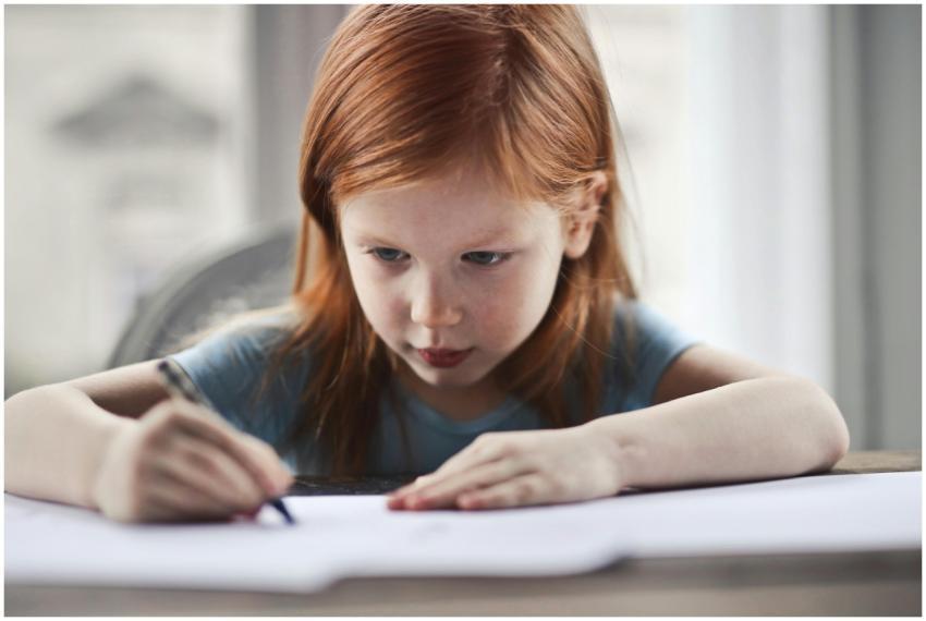 Focused young girl with red hair writing on paper