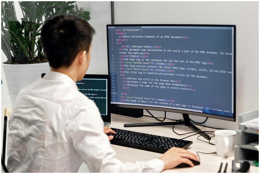 Adult male programmer coding on dual monitors in a