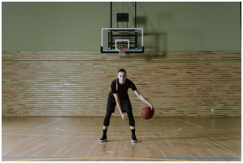 Focused young woman dribbling basketball in indoor