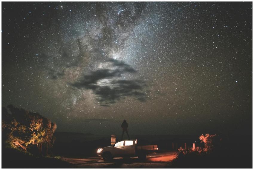 A silhouette on a car under a stunning starry sky