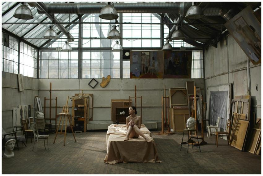 A woman poses nude in an industrial art studio, su