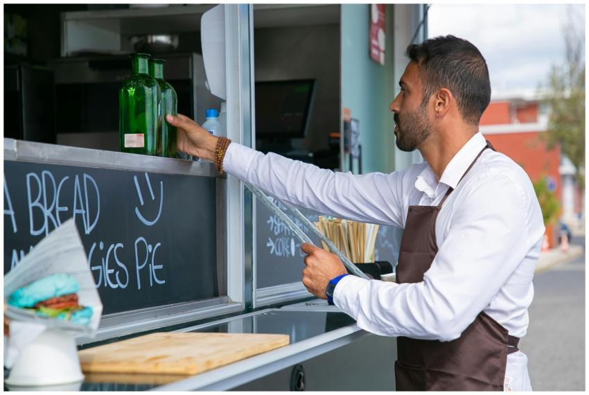 A male vendor in an apron prepares drinks at an ou