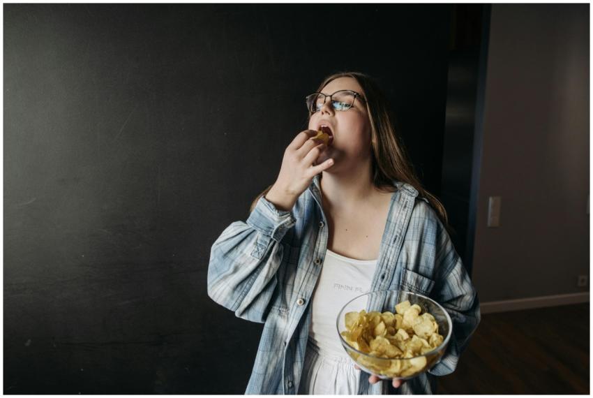 Young woman eating potato chips indoors, enjoying