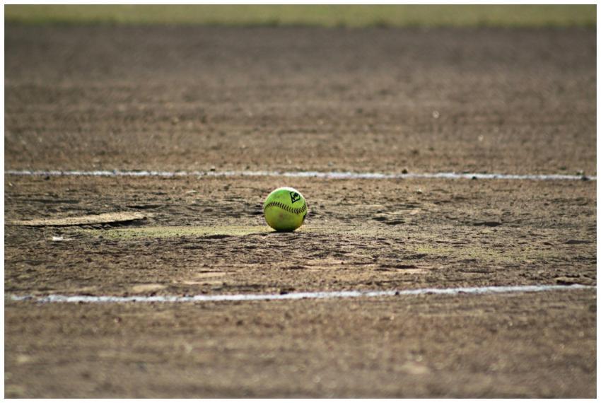A lone softball sits on a dusty field, capturing t