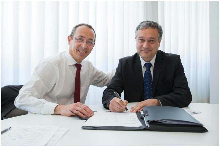 Two businessmen in suits signing a contract at a w