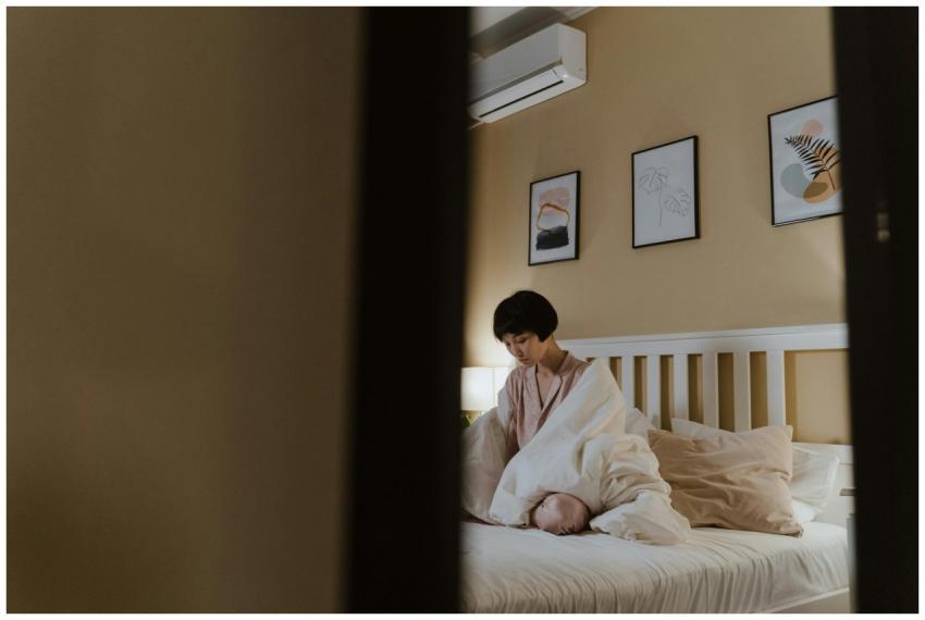 Asian woman sitting on bed, wrapped in blanket, in