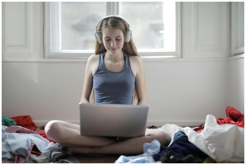Young woman sitting cross-legged on bed, using lap