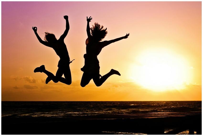 Silhouettes of two people joyfully jumping on a be