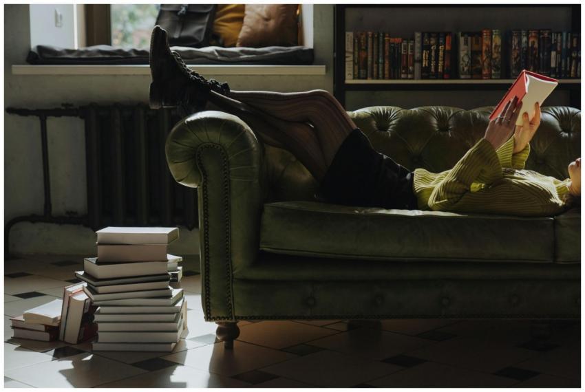 Person relaxing on a sofa reading a book indoors,
