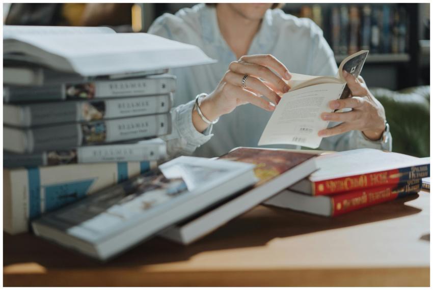 A young adult reading a book amidst a stack of boo