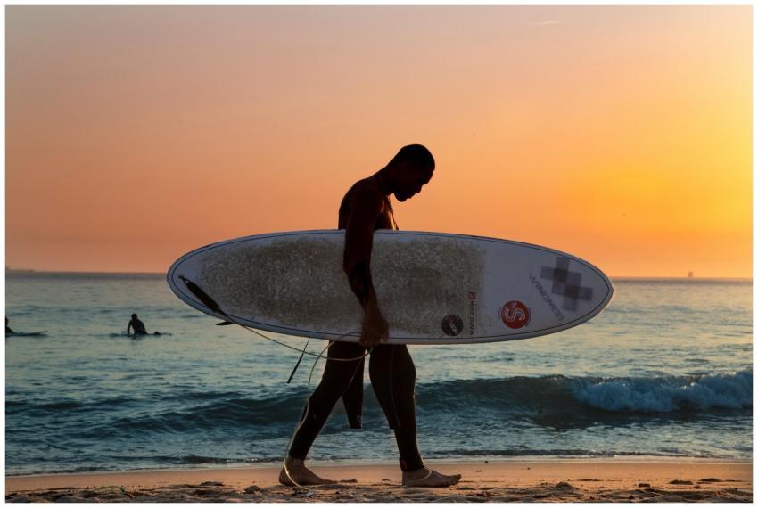 A surfer walks along Porto's beach with a surfboar