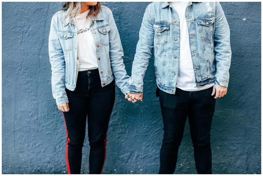 A fashionable couple holds hands against a blue wa