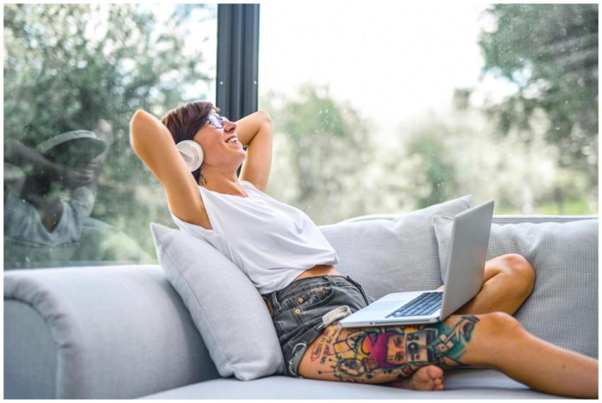 Woman reclining on a couch, using laptop while lis