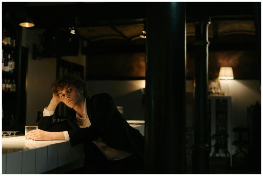 Young man in a black suit sitting alone at a bar,