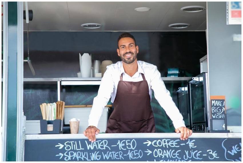 Good looking young waiter in apron standing at mod