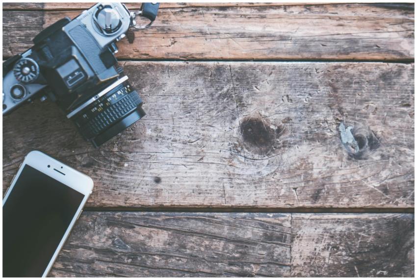A vintage camera and smartphone on a rustic wooden
