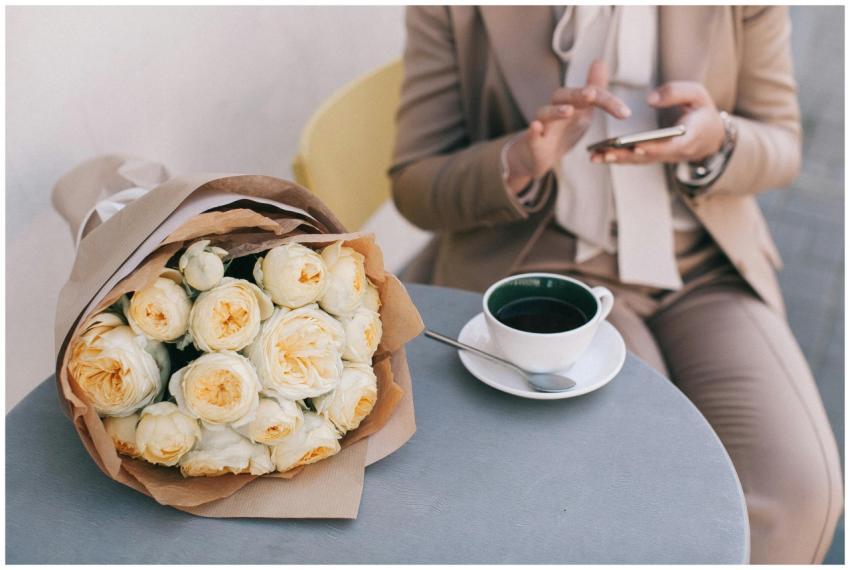 Stylish woman using phone beside bouquet and coffe