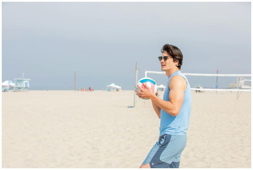 A young man in sunglasses holding a volleyball on