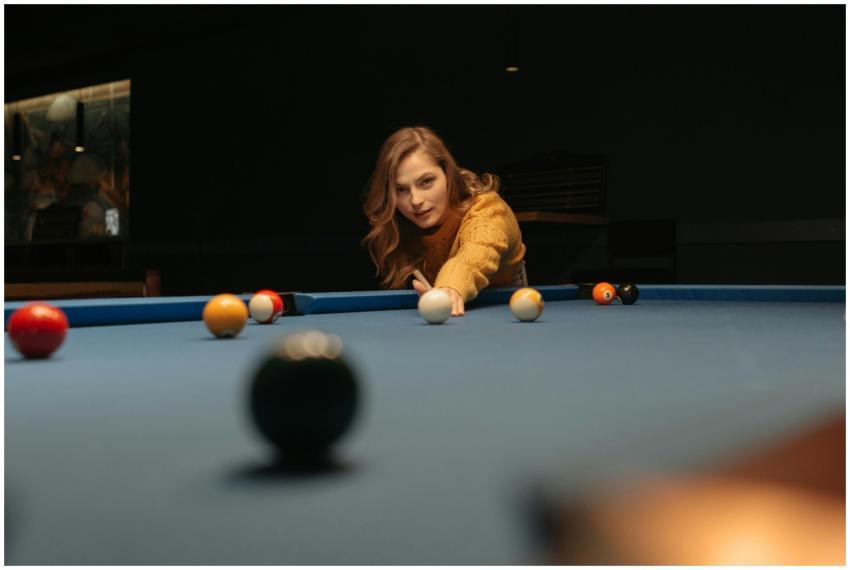A woman focuses on her shot while playing billiard