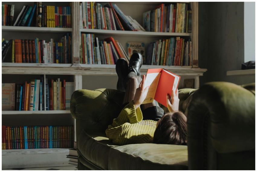 Young woman reading on a green sofa in a library,