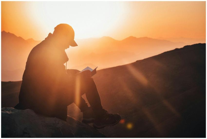 A man reads a book silhouetted against a vibrant s
