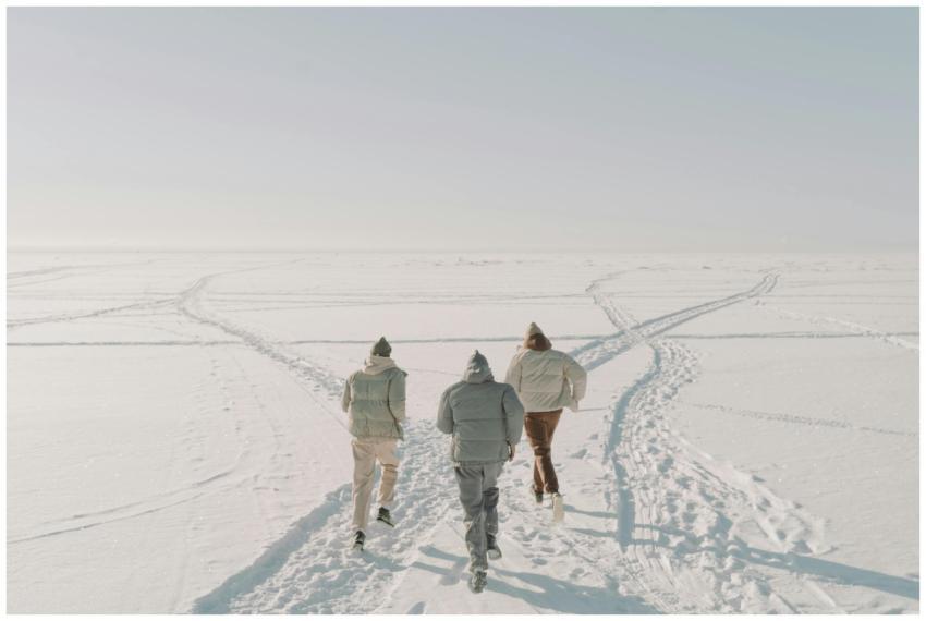 Three people running across a vast snowy field in