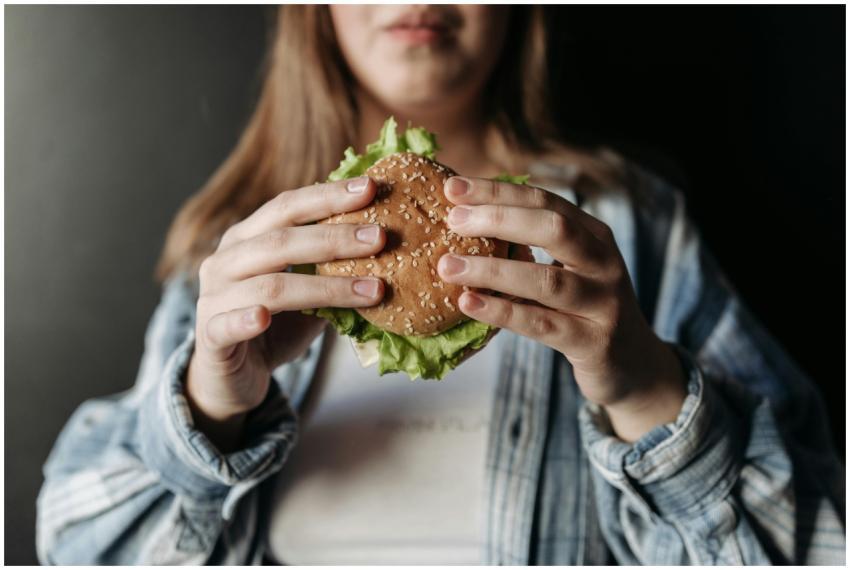 A person in a casual shirt holding a fresh burger