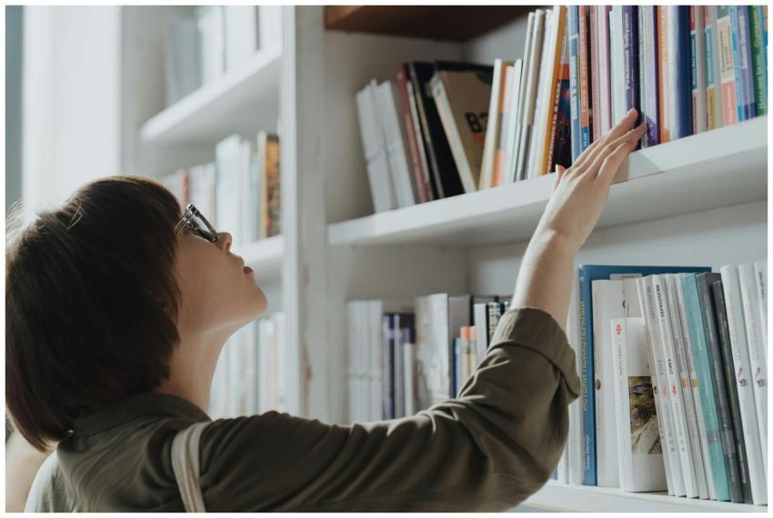 A woman wearing glasses browsing books on a librar