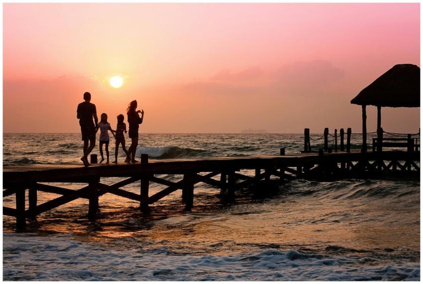 Silhouetted family enjoys a stroll on the beach pi