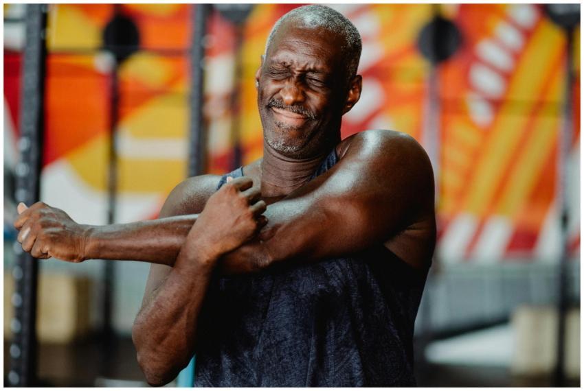 An elderly man stretches his arm indoors, embodyin