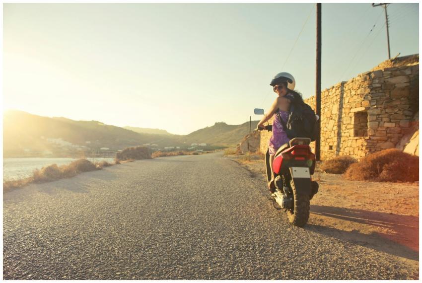 Woman riding scooter on scenic Greek road at sunri
