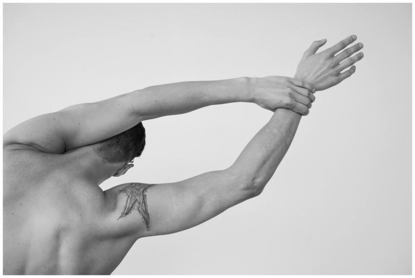 A tattooed man with short hair stretches his arms