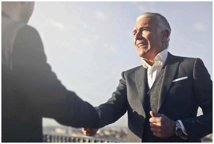 A senior businessman warmly shakes hands outdoors,
