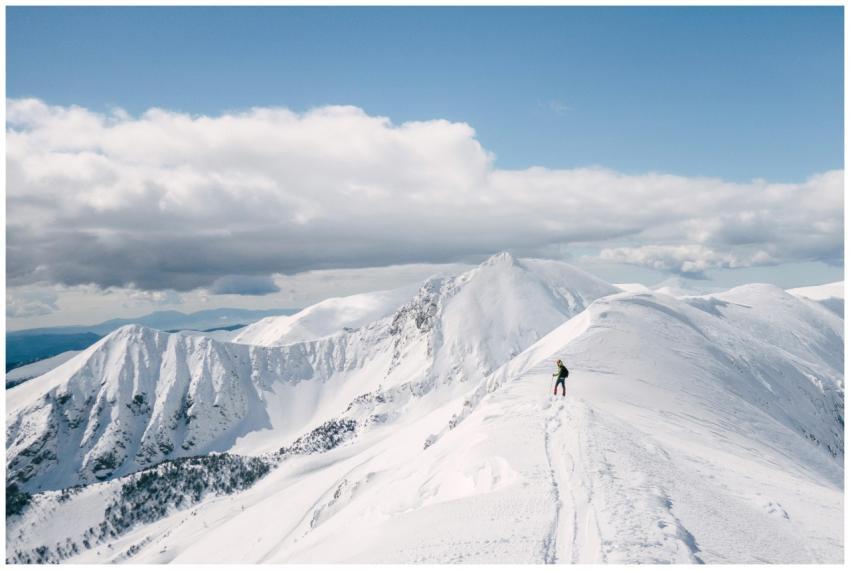 A lone hiker explores a snowy mountain ridge under