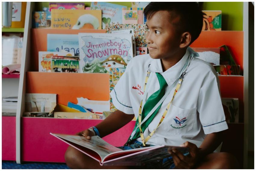 A young boy in a school uniform reads joyfully in
