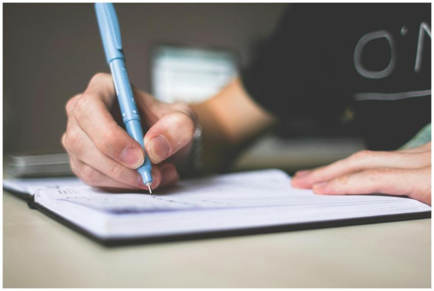 Close-up of hand writing in notebook using a blue