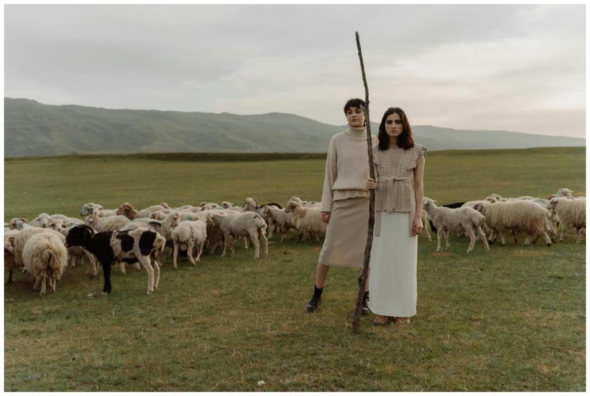 Two stylish women stand with sheep herd in pastora