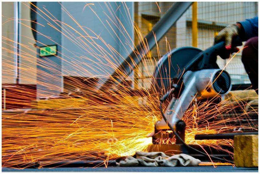 A worker operates a grinder cutting metal, creatin