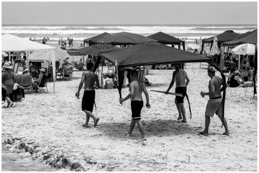 Monochrome beach scene with people carrying a cano