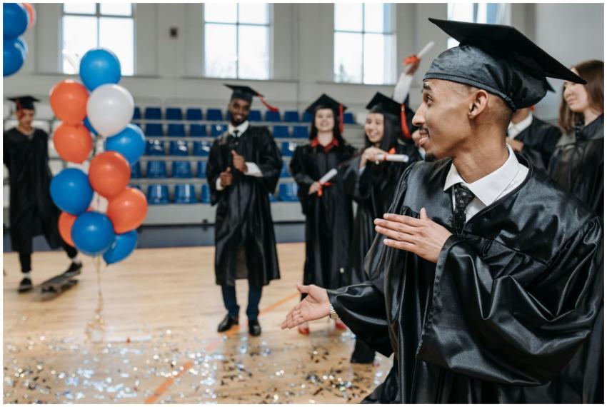 Happy graduates celebrating in a gym with balloons