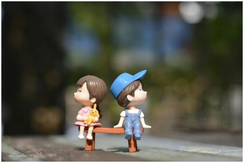Adorable figurines of a boy and girl sit on a benc