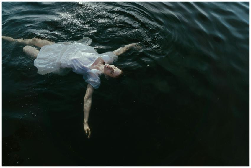 A woman in a white dress peacefully floats on a da