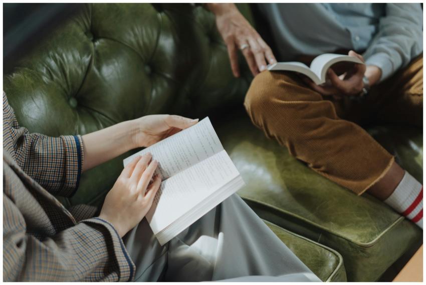 Two adults sitting on a sofa, engaged in reading b