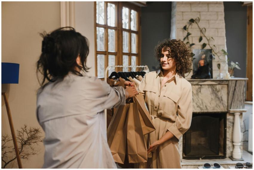 Two women in a boutique exchanging shopping bags w