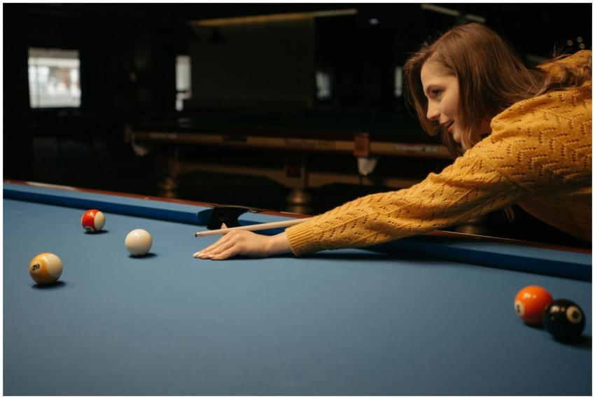 A woman in a knitted sweater plays pool on a blue