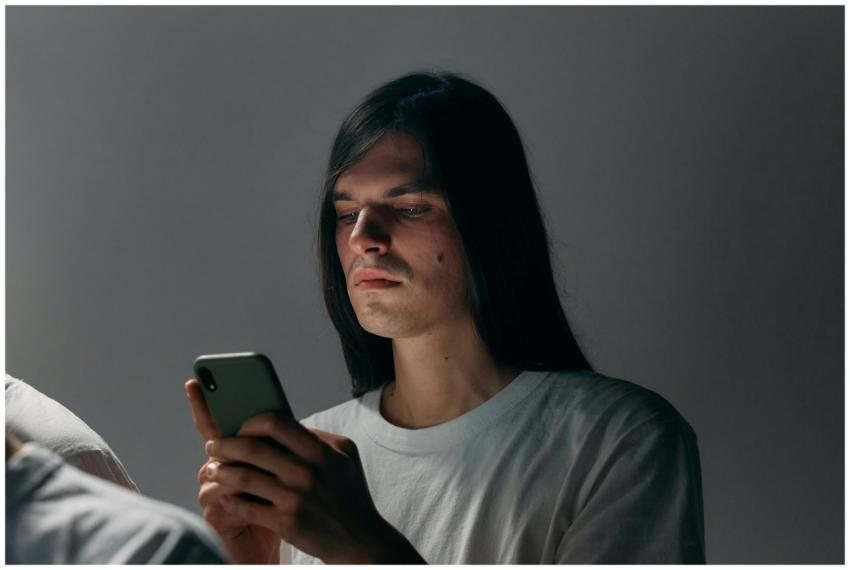 A young man with long hair focused on his smartpho