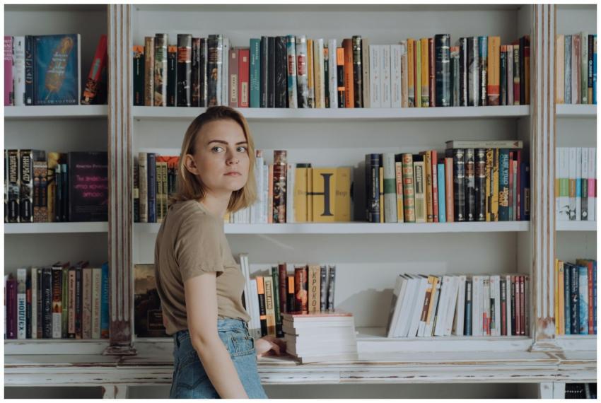 A young woman stands by bookshelves, surrounded by