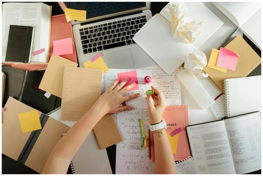 A cluttered desk with notebooks, sticky notes, and